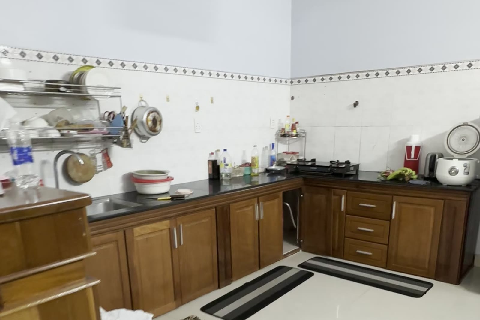 Khu bếp đóng gỗ chữ L với mặt đá đen, tủ trên tủ dưới, bếp gas và bồn rửa