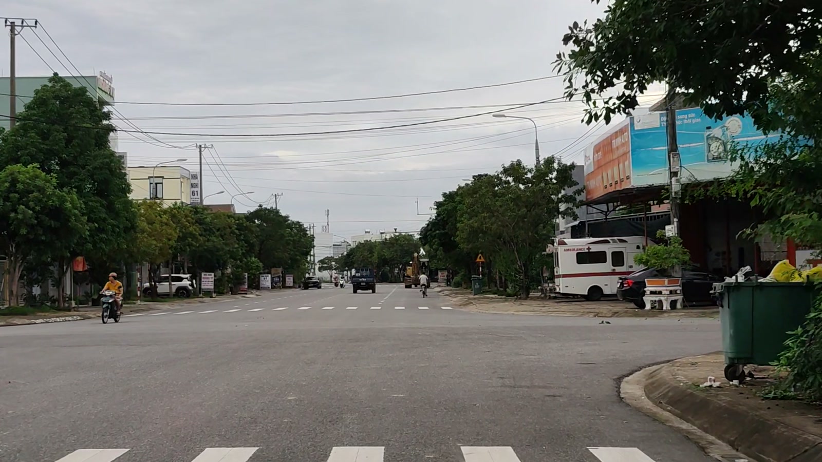 Dãy cửa hàng có bảng hiệu và nhà dân hai bên một con đường ở Tam Kỳ, xe máy chạy qua, ô tô đậu trước cửa hàng