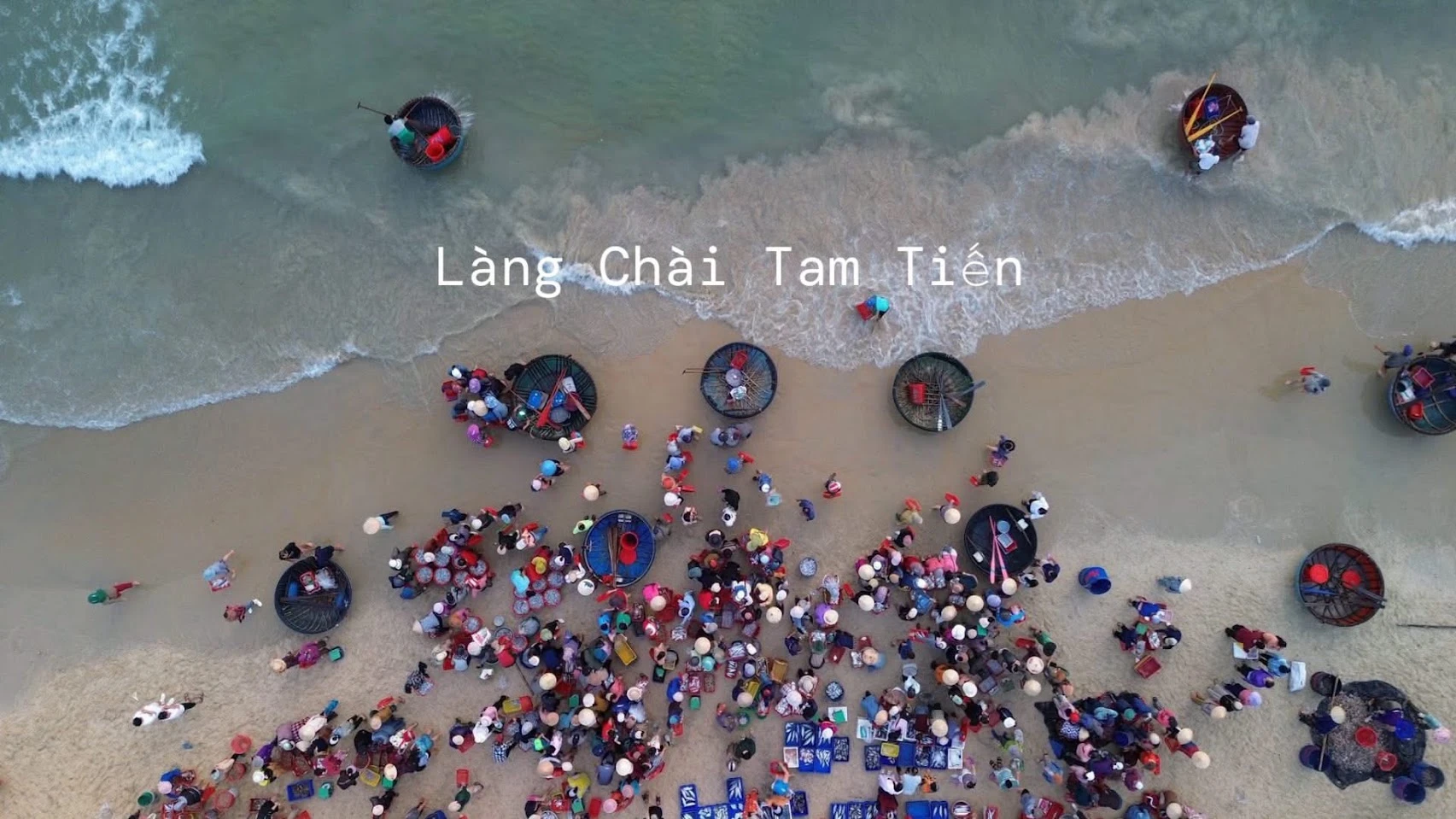 Chợ cá sáng sớm trên bãi biển Tam Tiến nhìn từ trên cao, hàng trăm người đội nón lá vây quanh các rổ cá, thúng chai đậu sát mép sóng
