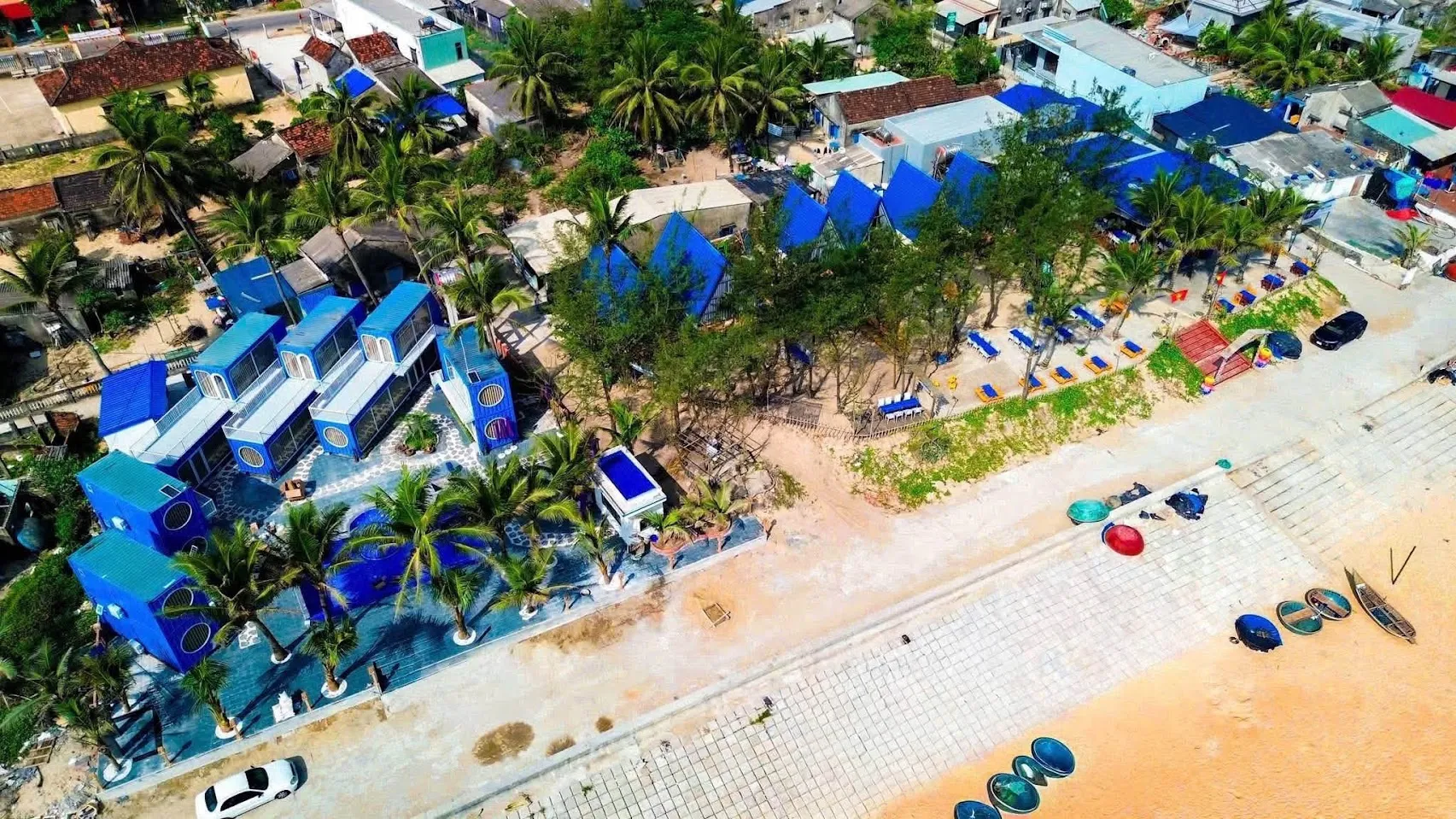 Khu lưu trú gồm các căn nhà lắp ghép sơn xanh dương nằm sát bãi biển, có hàng dừa, sân lát gạch và dãy ghế tắm nắng quay ra biển