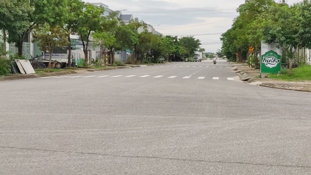 Con đường rộng có vạch qua đường và hàng cây xanh hai bên ở Tam Kỳ, dãy nhà phố phía xa
