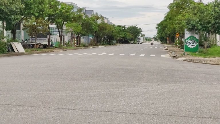 Con đường rộng có vạch qua đường và hàng cây xanh hai bên ở Tam Kỳ, dãy nhà phố phía xa