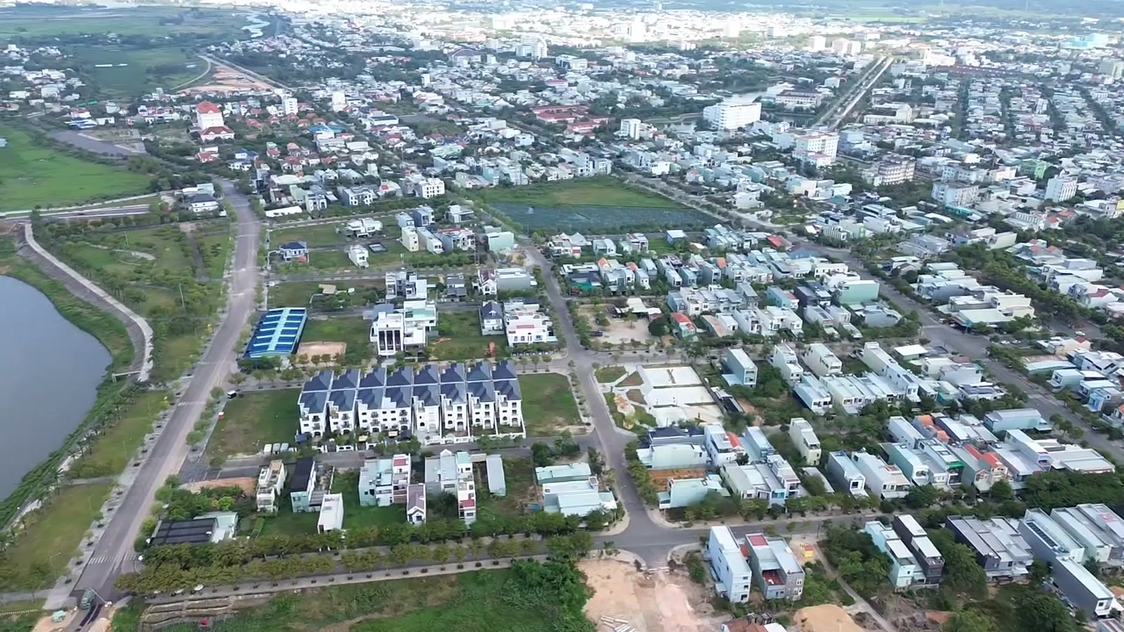 Nhà cửa hai bên một trục đường lớn ở Tam Kỳ nhìn từ trên cao bằng flycam, đường chạy thẳng giữa các dãy nhà phố và khu đất đang san nền