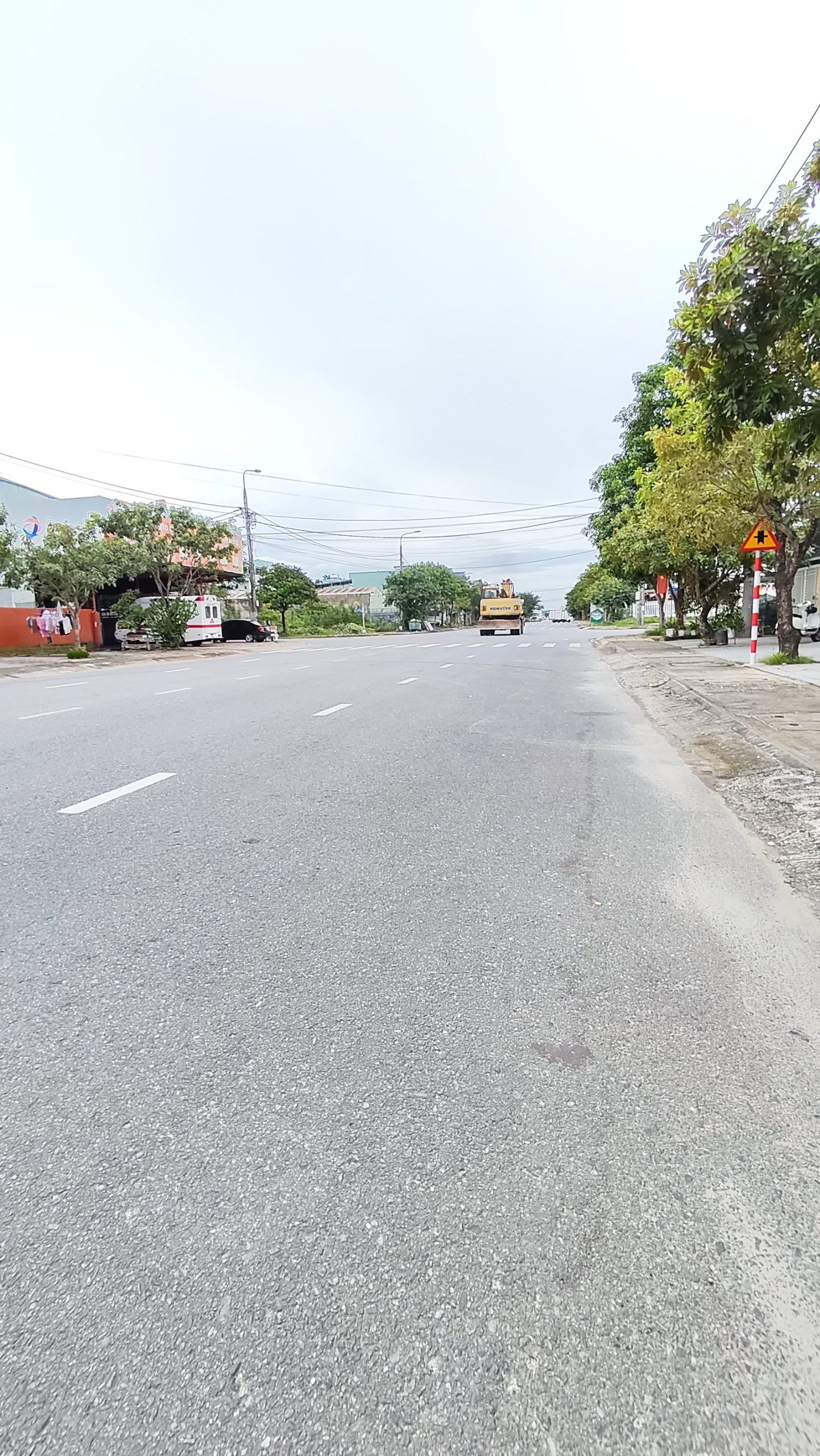 Mặt đường nhựa rộng chụp sát mặt đường, hàng cây xanh bên phải, xe lu làm đường ở phía xa