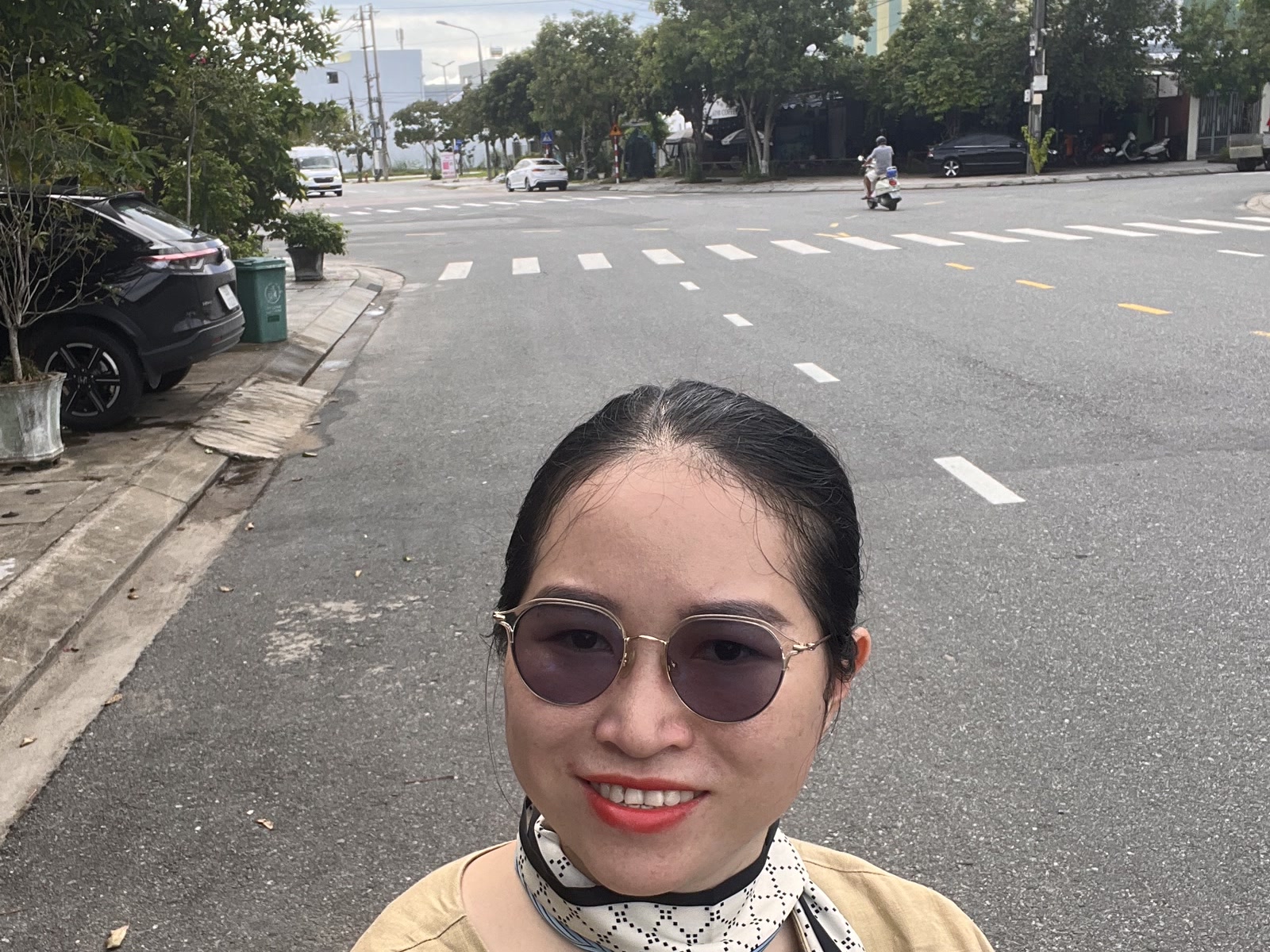 Nguyễn Thanh đứng giữa vỉa hè đường Lê Quý Đôn Tam Kỳ, phía sau là lòng đường rộng có vạch kẻ và hàng cây xanh hai bên