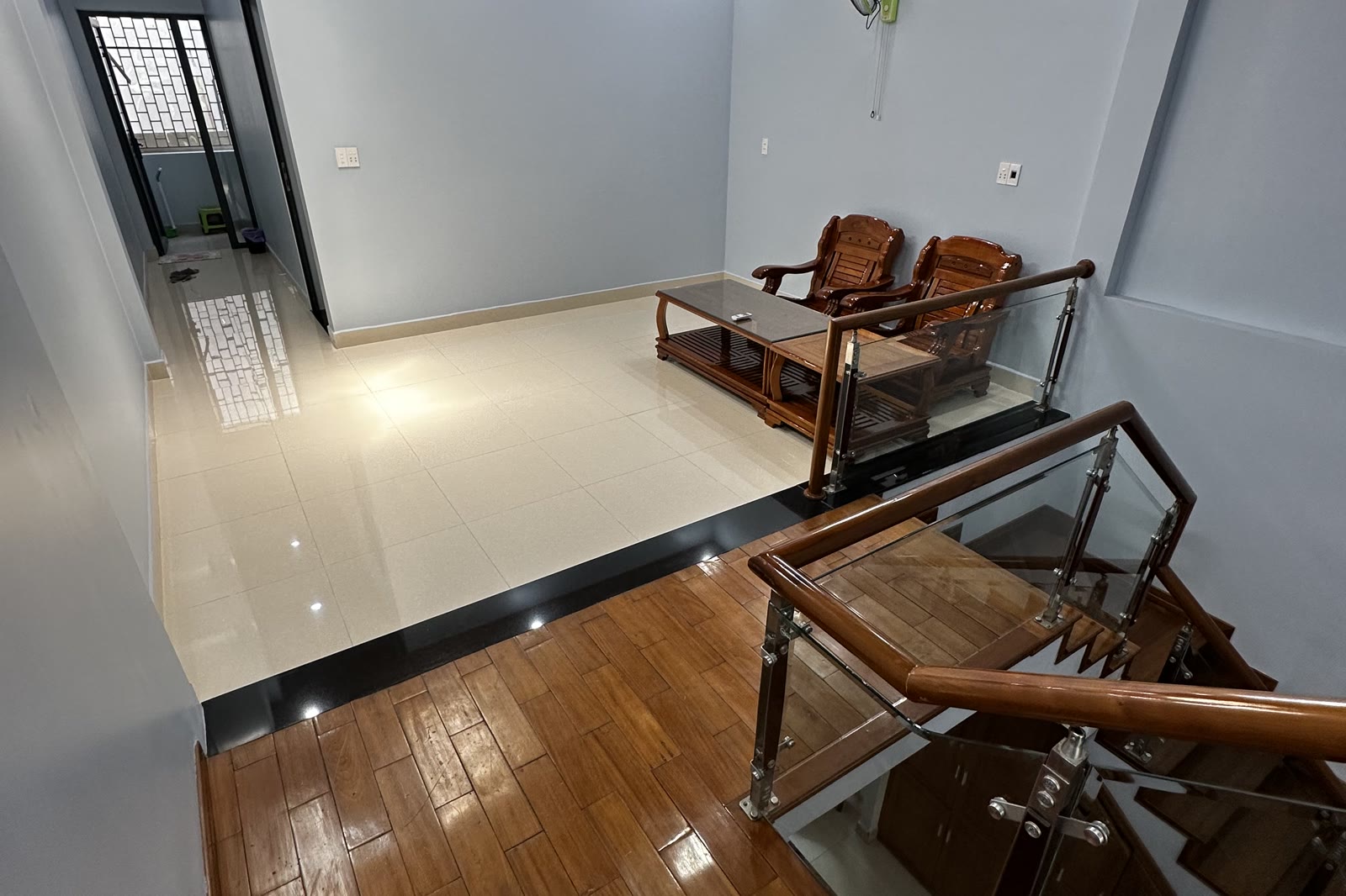 Khoảng sinh hoạt chung tầng hai lát sàn gỗ, có bộ bàn ghế gỗ tiếp khách và lan can kính nhìn xuống tầng trệt