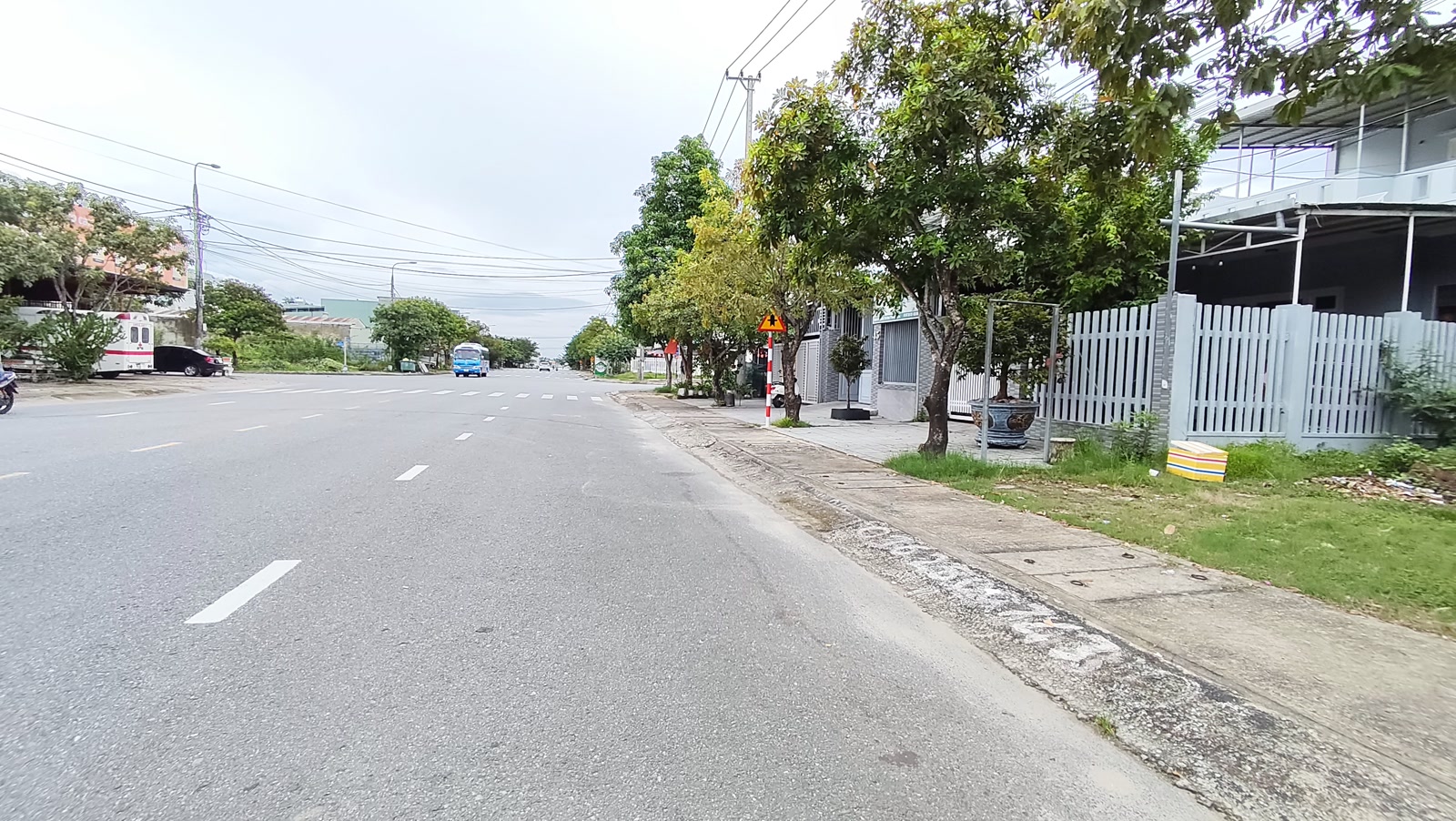Vỉa hè rộng lát gạch trước dãy nhà có hàng rào trên đường Lê Quý Đôn Tam Kỳ, hàng cây xanh trồng dọc lề