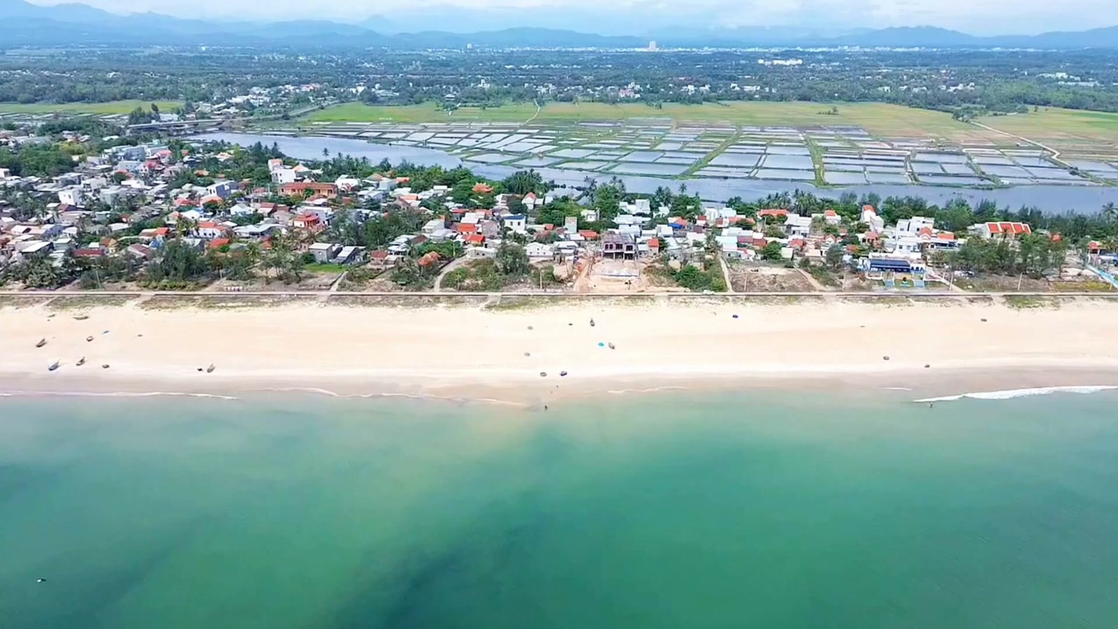 Bãi cát biển Tam Thanh trắng và dài, nước biển xanh trong, phía sau là làng và ô nuôi thuỷ sản