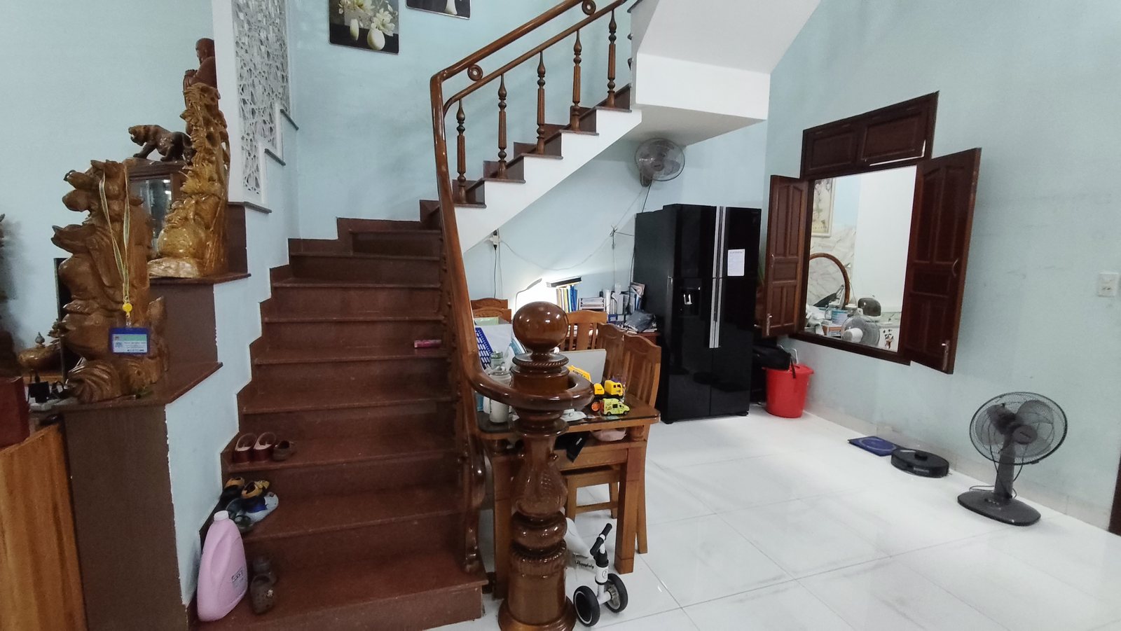 Cầu thang gỗ bậc lát đá đỏ, tủ lạnh và góc ăn đặt dưới chân cầu thang trong nhà 3 tầng Tam Kỳ