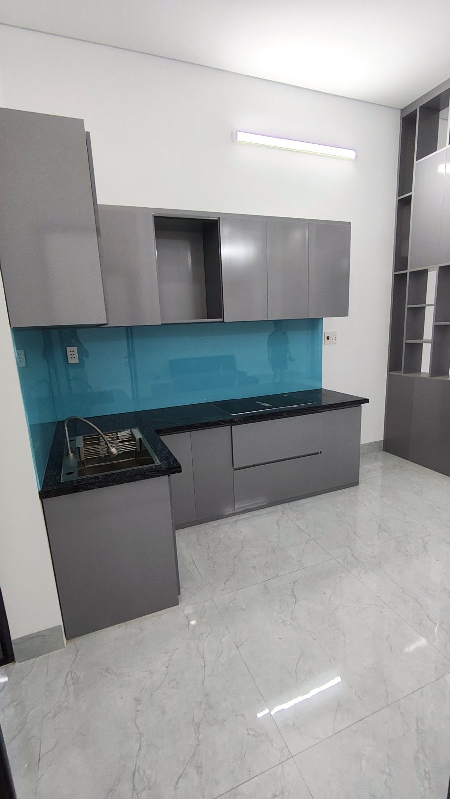 Bếp chữ L tủ xám mặt đá đen, tường ốp kính xanh ngọc, chậu rửa inox, nhà kiệt Trần Cao Vân Tam Kỳ