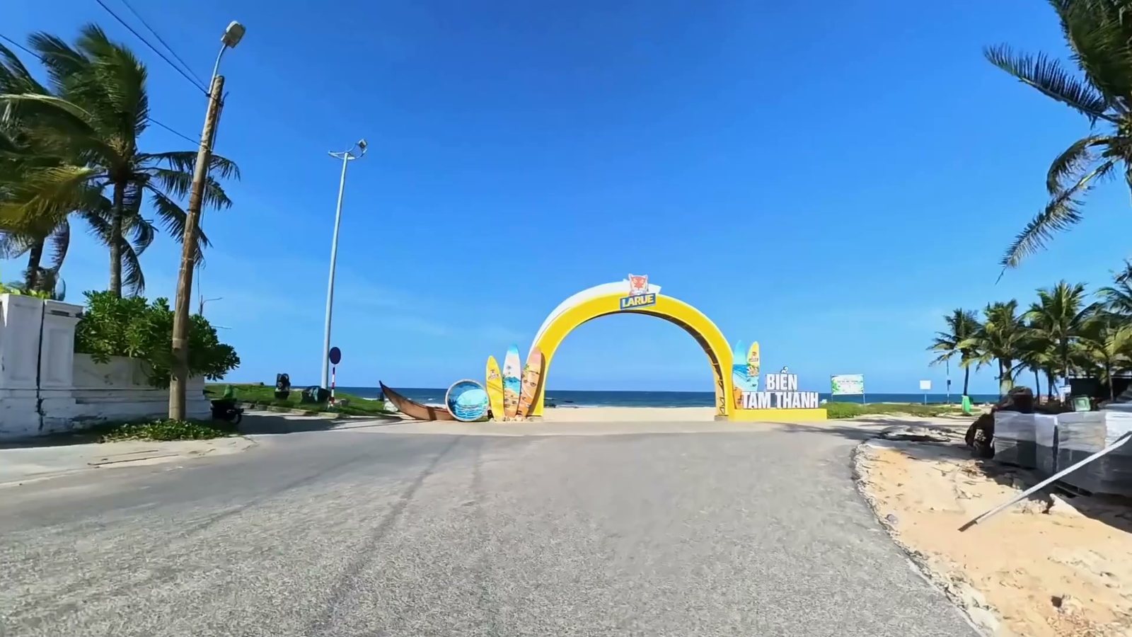 Cổng chào màu vàng dẫn xuống bãi biển Tam Thanh, hai bên đường có hàng dừa