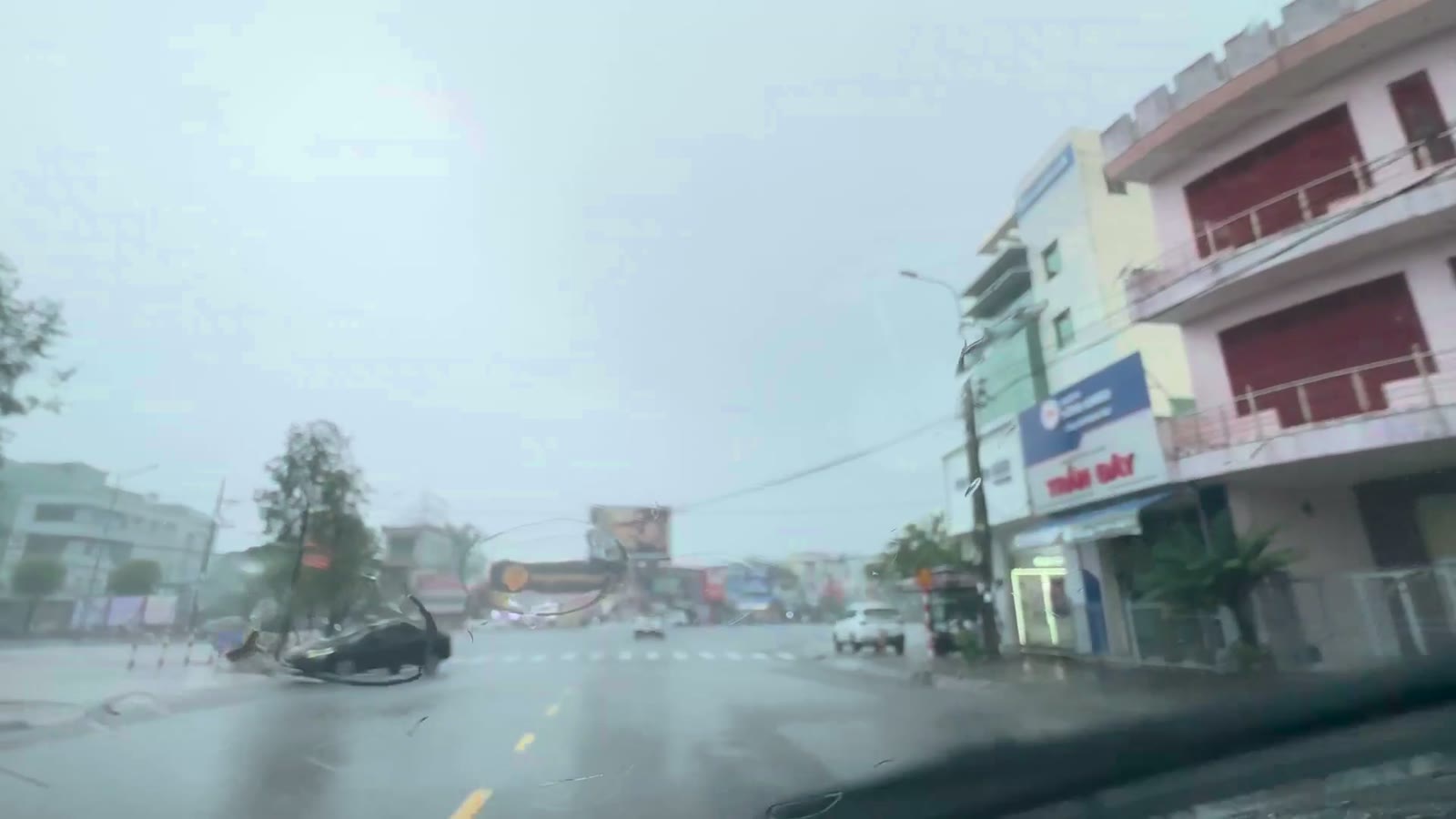 Đường đôi có dải phân cách trồng cây ở khu buôn bán Tam Kỳ trong sáng mưa lớn, mặt đường ướt nhưng nước vẫn chảy, không đọng