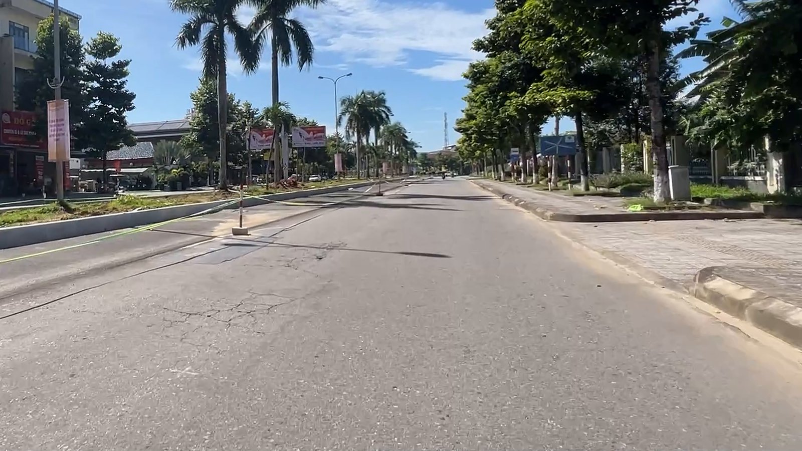 Mặt đường Hùng Vương Tam Kỳ rộng và vắng, hàng cọ hai bên, xe máy chạy phía xa