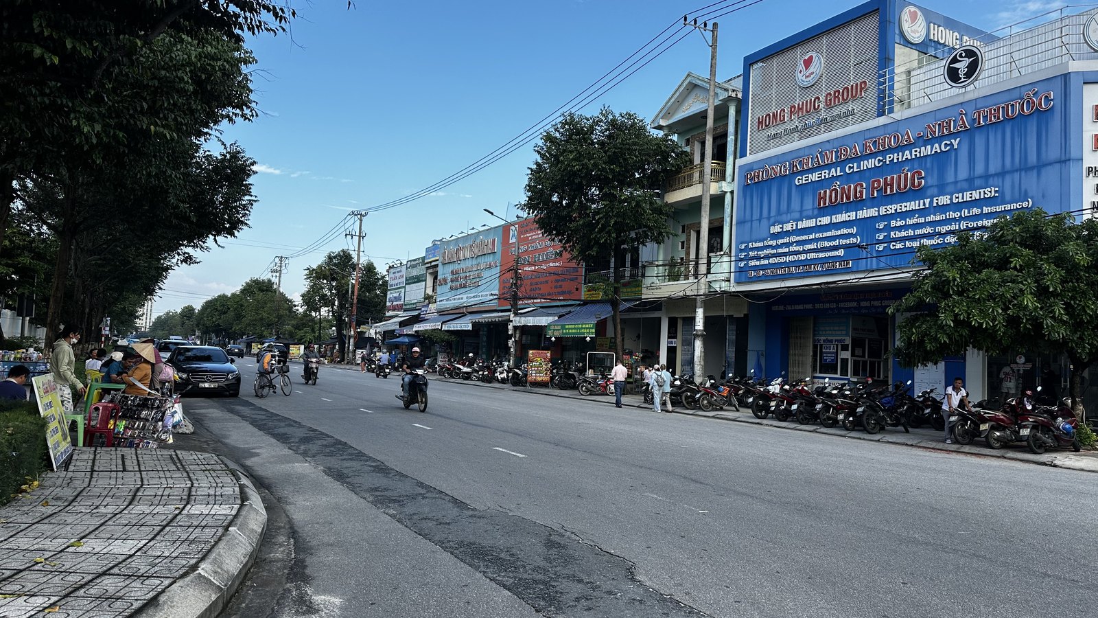 Dãy phố mặt tiền đường Nguyễn Du đoạn đối diện Bệnh viện Đa Khoa Tam Kỳ, có phòng khám, cửa hàng và xe máy đậu kín vỉa hè