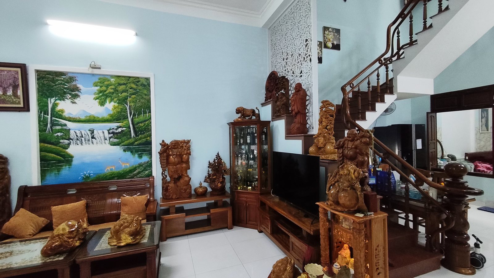 Phòng khách tầng trệt nhà góc 2 mặt tiền phường Bàn Thạch Tam Kỳ, bộ salon gỗ lớn, tranh sơn thủy, cầu thang gỗ phía sau