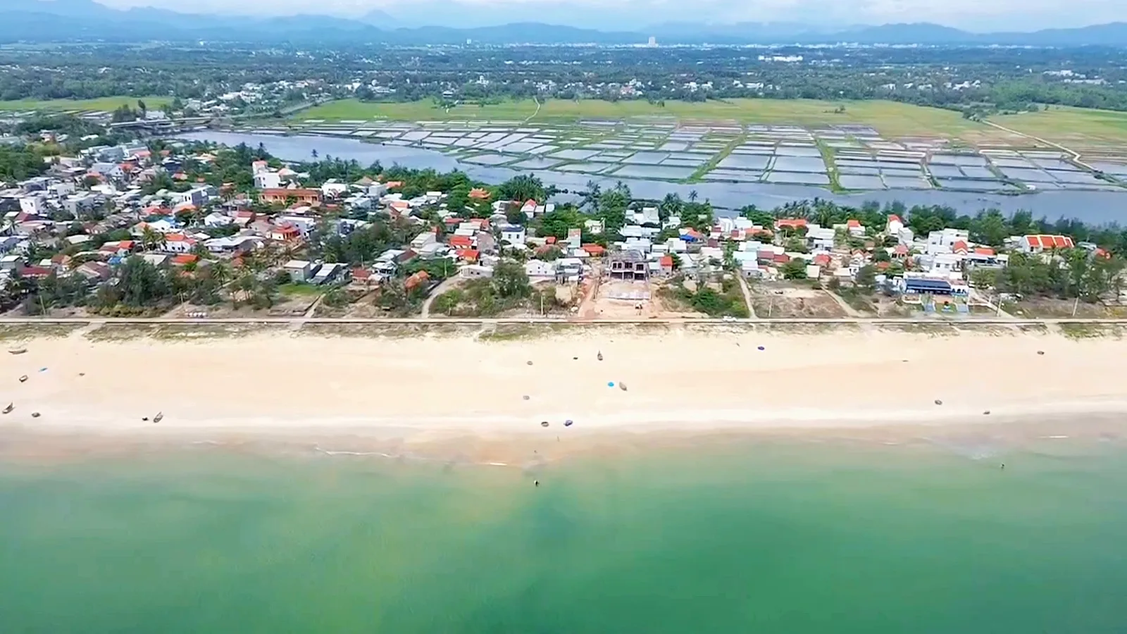 Làng chài Tam Thanh nhìn từ trên cao, bãi cát dài trước dãy nhà dân, phía sau làng là ruộng và ao nước
